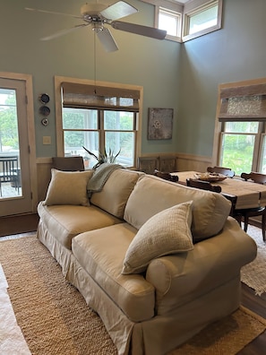 A living room with a beige sectional sofa, a ceiling fan, and a dining table with chairs.