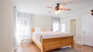 Quarto com cama de madeira, uma pequena mesa de cabeceira, um ventilador de teto e vista para uma porta.