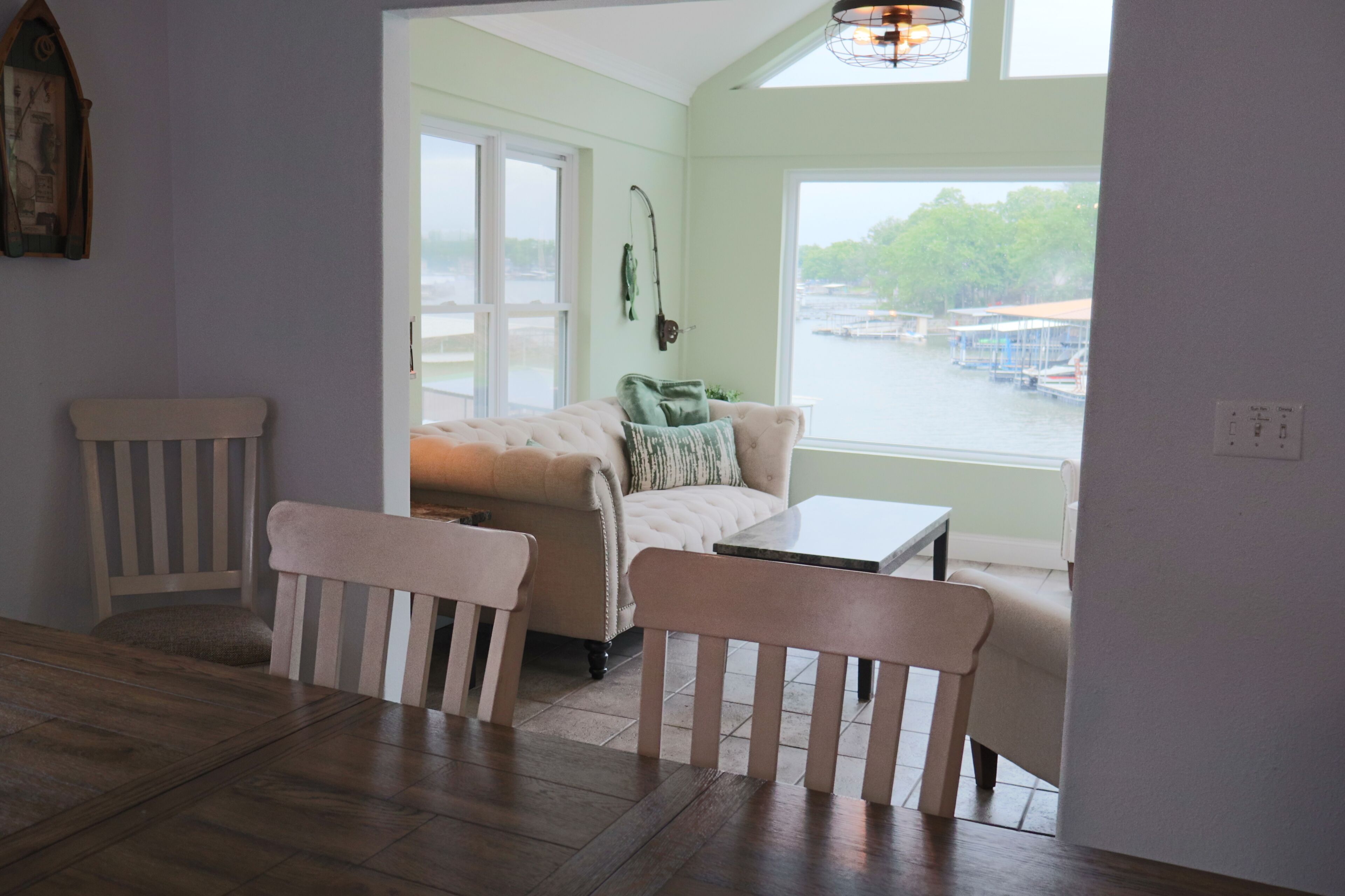 Une pièce comprenant un canapé, deux fauteuils, une petite table, une fenêtre donnant sur le port et un luminaire fixé au mur.