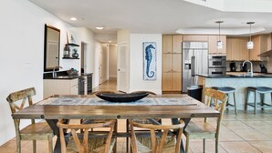 A modern kitchen with wooden cabinets, stainless steel appliances, and a dining area with a wooden table and chairs. - Caribe Resort C315 | Gorgeous 3/3 plus Media/Bunk Room! (Orange Beach)