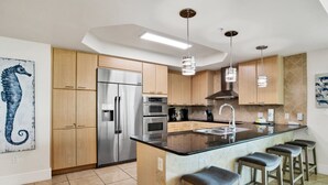 A modern kitchen with a central island, stainless steel appliances, wooden cabinets, and pendant lighting. - Caribe Resort C315 | Gorgeous 3/3 plus Media/Bunk Room! (Orange Beach)