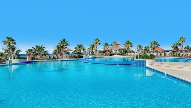 A clear blue pool with lounge chairs and palm trees. - Caribe Resort C315 | Gorgeous 3/3 plus Media/Bunk Room! (Orange Beach)
