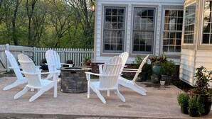 A patio with four Adirondack chairs, a stone fire table, and potted plants. - Special Rates-Enjoy Hot Springs in Our Colonial Williamsburg Reproduction Home (Hot Springs)