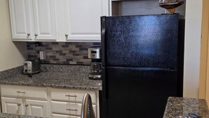 A kitchen with white cabinets, a black refrigerator, granite countertops, and a small sailboat decoration. - Beautiful Condo - Water View Near City Dock  (Annapolis)
