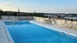 A rooftop pool with clear blue water, surrounded by lounge chairs and a view of a cityscape including a church and marina. - Beautiful Condo - Water View Near City Dock  (Annapolis)
