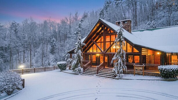 A log cabin with a large front porch, surrounded by snow-covered trees. - Swim Spa Pool - Hot Tub - Theater & Game Room - 5 mins to Pigeon Forge (Pigeon Forge)