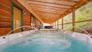 A wooden cabin with a hot tub under a covered area. - Swim Spa Pool - Hot Tub - Theater & Game Room - 5 mins to Pigeon Forge (Pigeon Forge)