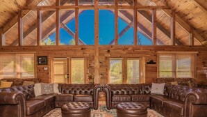 A log cabin interior with a large sectional sofa, ottomans, and a patterned rug. - Swim Spa Pool - Hot Tub - Theater & Game Room - 5 mins to Pigeon Forge (Pigeon Forge)
