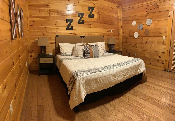 A wooden cabin bedroom with a bed, nightstands, and wall decorations including 'Z' letters and circular patterns.