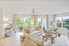Relax in this serene space with a white sofa, armchair, and wicker sofa, surrounded by lush views.