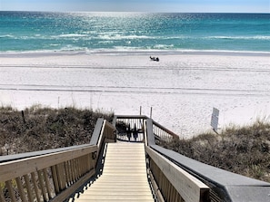 A wooden boardwalk leading to a beach with clear turquoise water and a sandy shore.