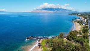 Zona costera con playa, una montaña al fondo y una carretera bordeada por edificios.