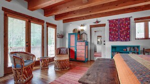 A spacious room with wooden floors, a large wooden table, wicker chairs, a colorful rug, a bookshelf, and a door leading to another room.