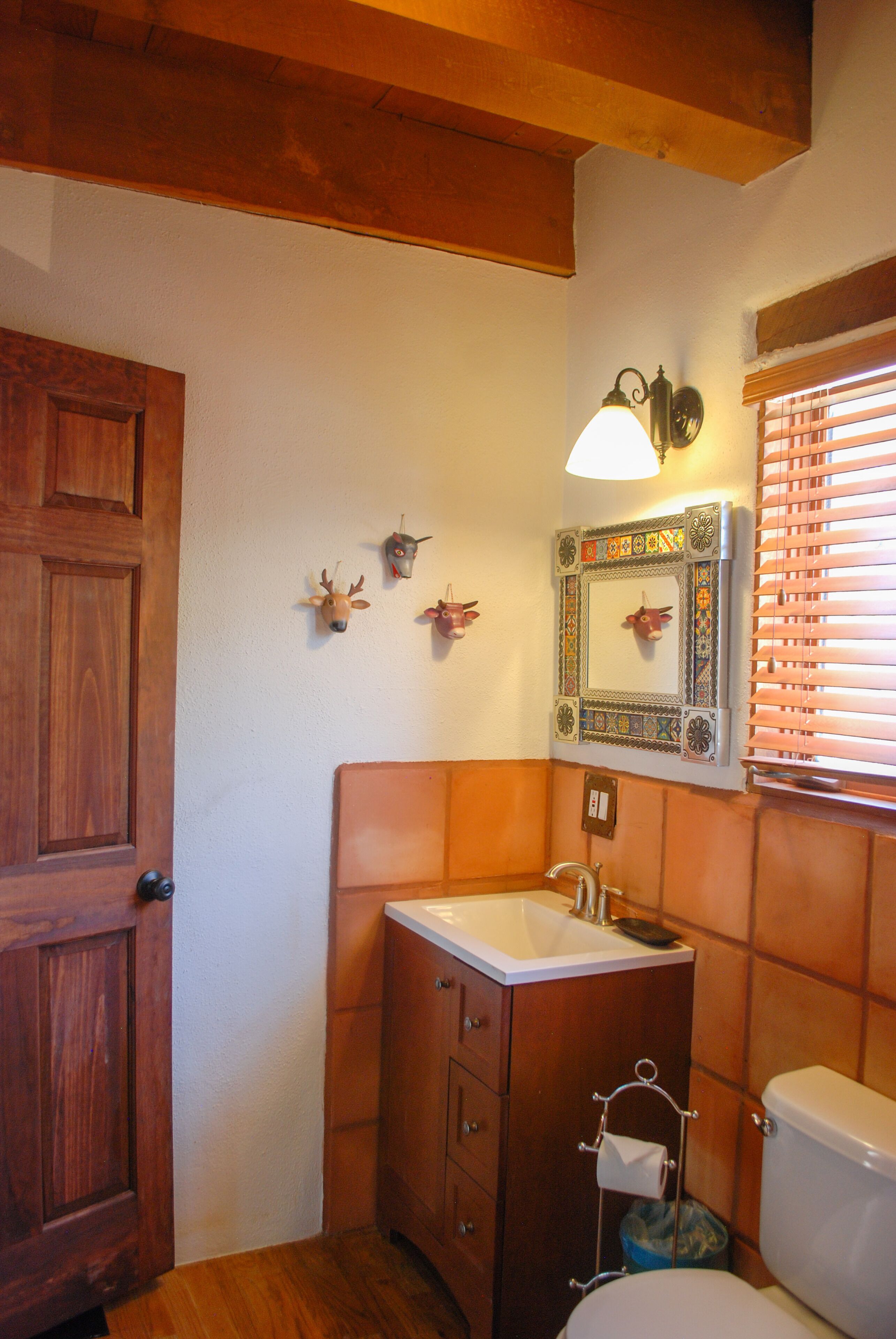 A bathroom with wooden cabinetry, a white sink, a mirror with a decorative frame, and a window with blinds.