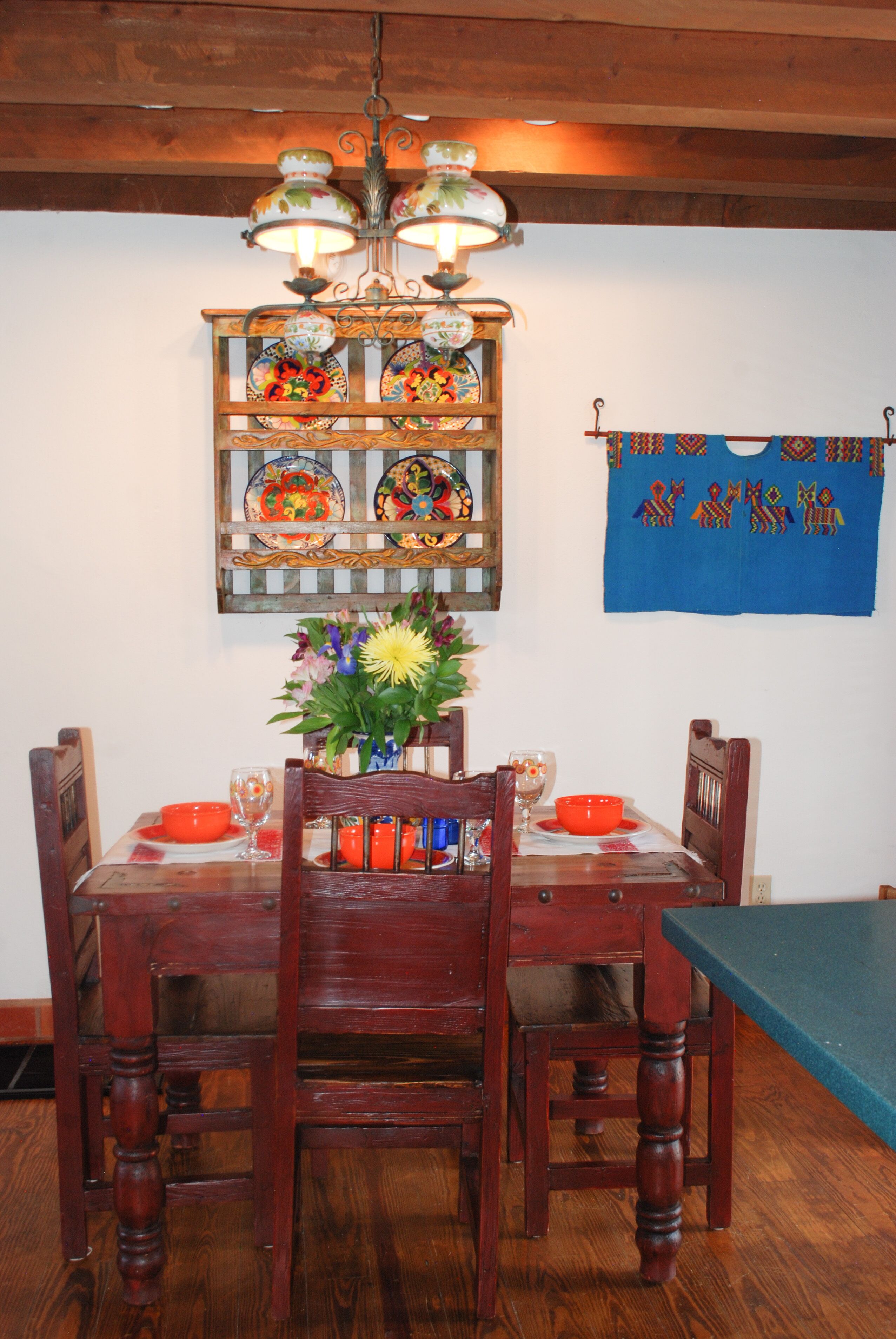A dining table with chairs, a chandelier, a wall-mounted decorative plate rack, and a blue cloth hanging on the wall.