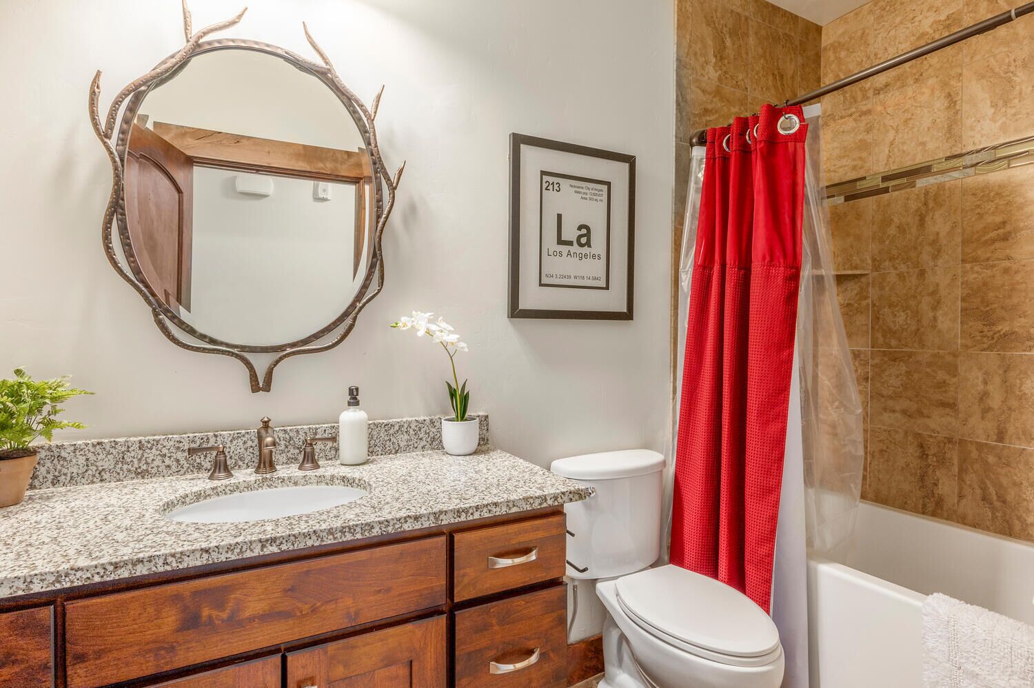 A bathroom with a vanity, two sinks, a toilet, a shower curtain, a mirror, and a framed sign.