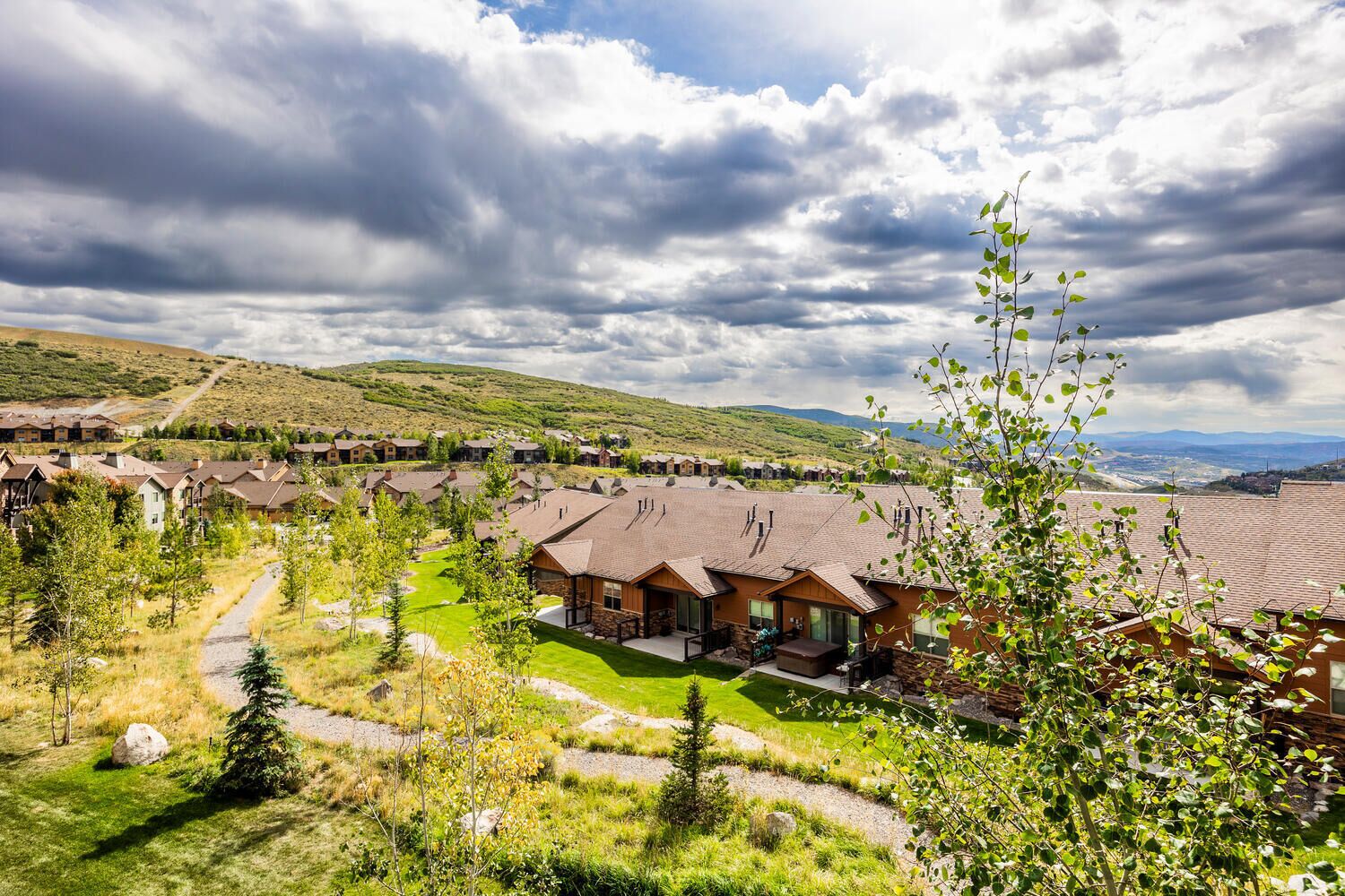 A residential area with houses, a well-maintained lawn, and a hilly landscape in the background.