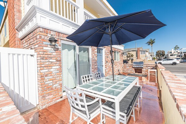 Un patio con una mesa y sillas de vidrio, una sombrilla azul y un muro de ladrillo.