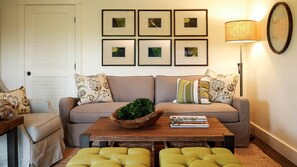A living room with a sofa, two armchairs, a coffee table with a plant, framed pictures on the wall, and a lamp.