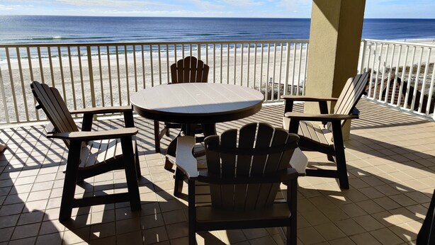 Un espace extérieur abrité, avec une table ronde et quatre chaises Adirondack, donnant sur une plage, une rambarde et offrant une vue sur l’océan.