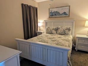 A bedroom with a bed, a nightstand, a lamp, a dresser, and a painting on the wall.