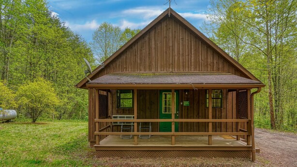 Een houten hut met een veranda, een groene deur en een schotelantenne.