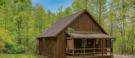 Une cabane en bois avec un porche, entourée d’arbres.