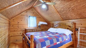 Een slaapkamer in een houten hut met een bed, nachtkastje, lamp en plafondventilator.