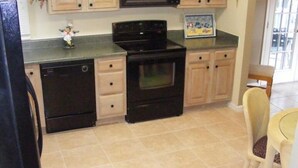 A kitchen with a black dishwasher, stove, and oven, wooden cabinets, and a tiled floor.