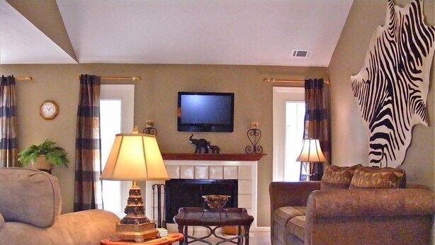 A living room with a fireplace, a television mounted above it, and a zebra skin on the wall.