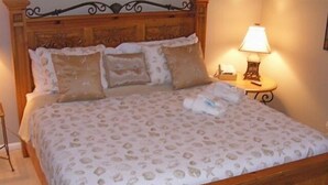 A bed with a patterned bedspread, pillows, and a bedside table with a lamp.