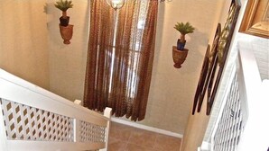 A staircase with a white railing, brown patterned curtains, and potted plants on the walls.