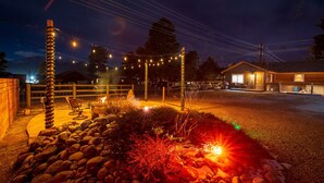 Un espacio exterior bien iluminado con cerca de madera, luces colgantes y una pequeña zona de estar.