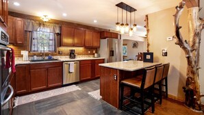 Una cocina moderna con armarios de madera, una isla central con taburetes y un horno empotrado, además de una lámpara colgante.