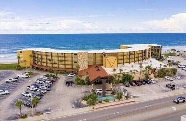 A large hotel with a curved facade, a parking lot, and a view of the ocean.