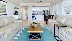 A modern living room with two white leather sofas, a wooden coffee table, and a blue patterned rug.