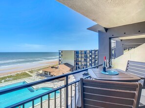 Ein Balkon mit Blick auf Strand und Meer, ein Pool sowie ein Tisch mit Flasche und Glas.