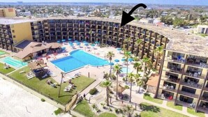 A resort with a large central pool, multiple balconies, and a view of the surrounding area.
