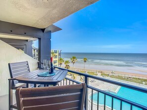Un balcon avec une table et des chaises, donnant sur une plage et une piscine.