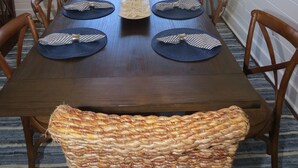 Comedor con mesa de madera dispuesta para seis personas, un banco tejido y una araña.