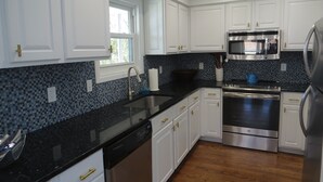 Una cocina moderna con armarios blancos, encimera negra, electrodomésticos de acero inoxidable y un salpicadero de mosaico azul.