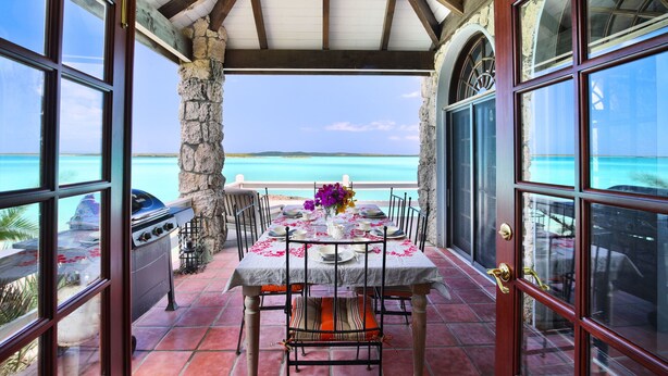 Un patio abierto con una mesa lista para comer, con vista al mar turquesa.