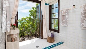 Un baño con vistas al verde exterior, una ventana con un perchero y un estante de mimbre con toallas.