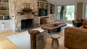 A living room with a stone fireplace, a television, and a large window offering a view of the outdoors.