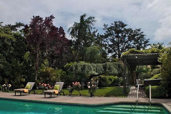 A swimming pool with lounge chairs, a pergola, and lush greenery.