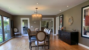 A spacious dining area with a wooden table and chairs, a chandelier, and a view through large windows.