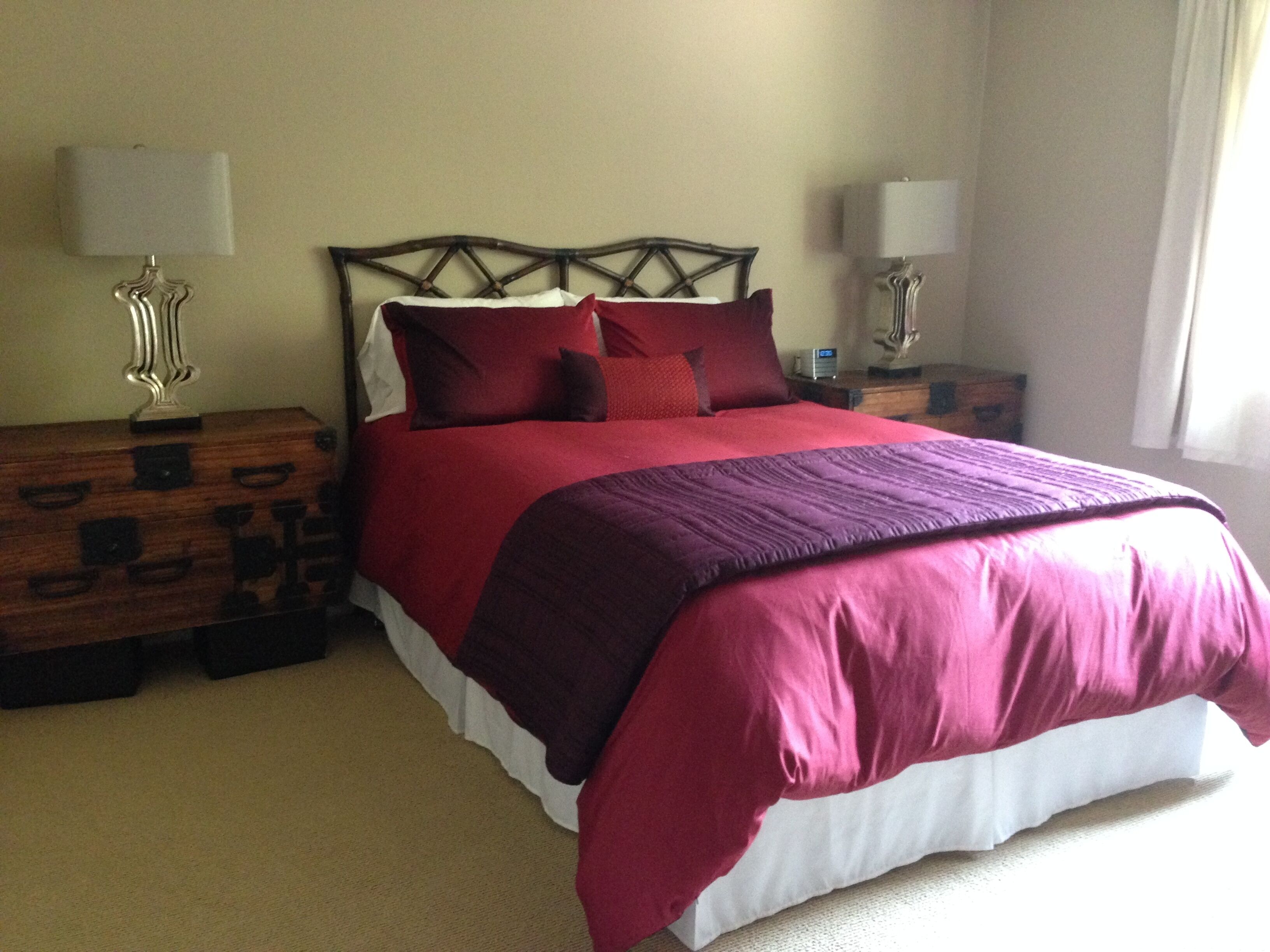 A neatly made bed with a wooden headboard, two bedside tables with lamps, and a beige carpet.