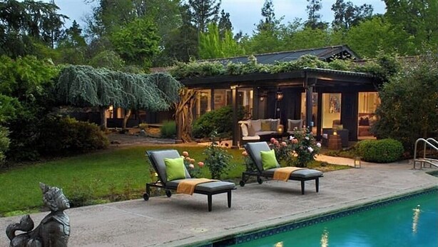 A poolside area with lounge chairs and a small house with a covered patio.