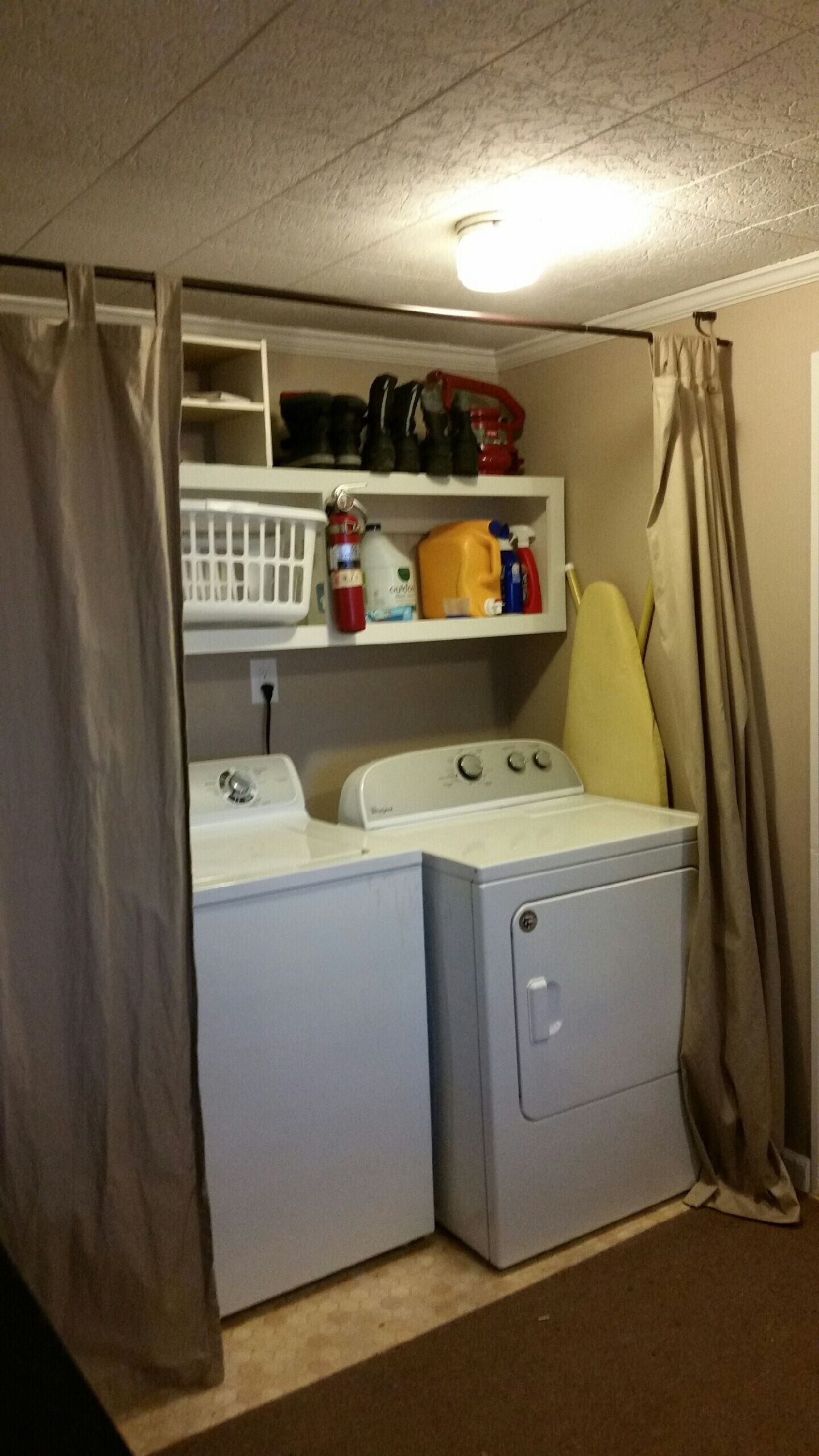 A laundry room with a washing machine, dryer, and shelves above containing cleaning supplies.