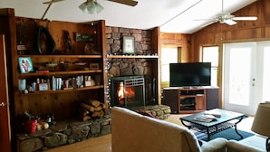 A cozy living room with a stone fireplace, wooden shelves, a television, and a ceiling fan. - Million-Dollar Views, spectacular! Sugar Mountain Cabin 3 Bedrms 3 bath sleeps 7 (Sugar Mountain)